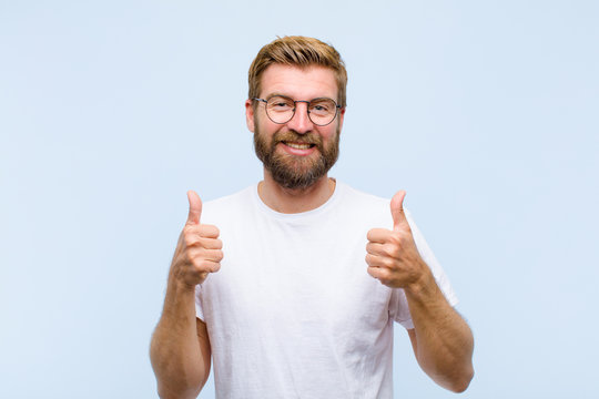young blonde adult man smiling broadly looking happy, positive, confident and successful, with both thumbs up