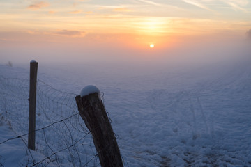Hazy sunset over a snowy field, with fence in the foreground.