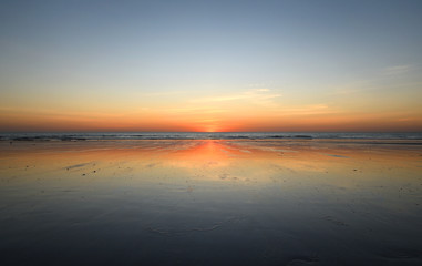 Obraz premium Beach horizon looking out to sea with glowing warm sunset reflecting on wet sand foreground.
