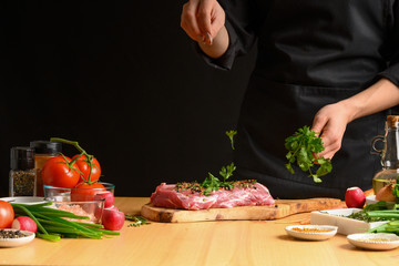 Pork steak and green herbs, Italian parsley from the chef in the background. Horizontal photo. With vegetables, tomatoes, hot peppers, onions and a chapel. With black background