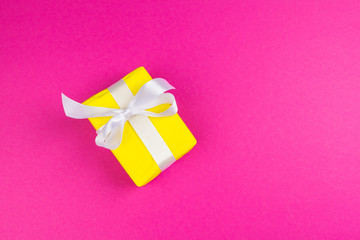 Top view of a decorated present with a bow on pink background