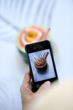 Top view of woman hand hold smart phone taking picture of beautiful cocktail made from whole watermelon.