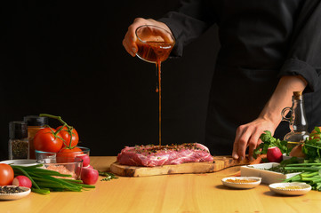 Chef cooks pork steak. pouring sauce, marinade on a background with vegetables. Recipe book, cooking, restaurant business - obrazy, fototapety, plakaty