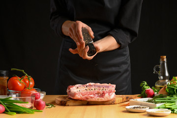 Chef cooks pork ribs. sprinkling with pepper on a background with vegetables. Freezing in motion. Recipe book, cooking, restaurant business