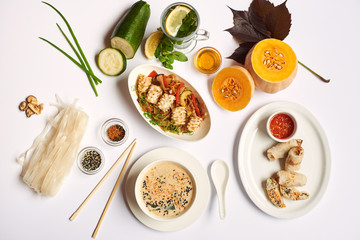 Flat lay of oriental dinner from soup with seeds, tempura shrimps and noodles with vegetables preparing for client. Three dishes lunch with mint tea ready for eating on white tablecloth.