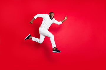 Fototapeta na wymiar Full length profile photo of excited dark skin man jump high running x-mas shopping need buy many presents wear white sweater trousers isolated red background