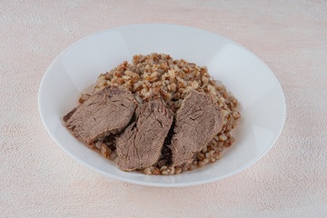 Buckwheat porridge with three pieces of boiled beef on a white plate, light background.