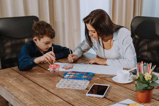 Portrait of a mature woman spending time with her son painting together for a school project , very attractive people in a modern house