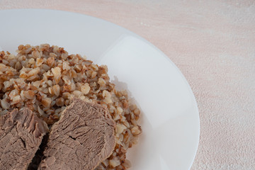 Buckwheat porridge with three pieces of boiled beef on a white plate, light background.