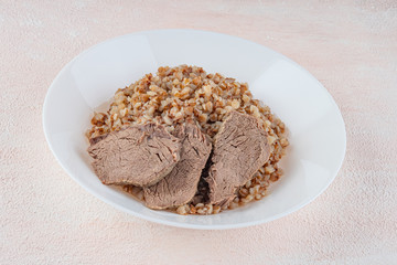Buckwheat porridge with three pieces of boiled beef on a white plate, light background.