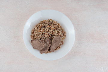 Buckwheat porridge with three pieces of boiled beef on a white plate, light background.