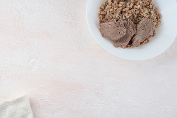 Buckwheat porridge with three pieces of boiled beef on a white plate, light background.