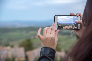 Detail of the hands of a girl taking a picture from her smartphone. In the background a countryside panorama.