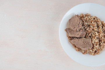 Buckwheat porridge with three pieces of boiled beef on a white plate, light background.