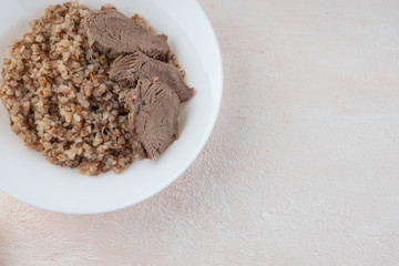 Buckwheat porridge with three pieces of boiled beef on a white plate, light background.