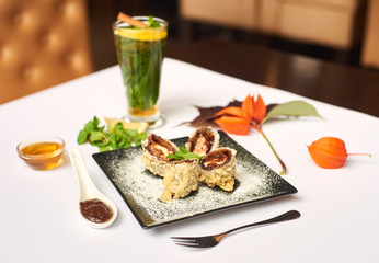 Delicious dessert on black plate decorated with physalis prepared for client. Sweet sushi roll cooking in oil with chocolate sauce and icing sugar doing by special recipe. Tasting best with mint tea.