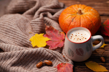 Pumpkin spiced latte or coffee in glass decorated knitted scarf on vintage background. Autumn, fall or winter hot drink.