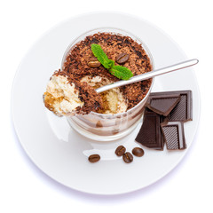 Classic tiramisu dessert in a glass cup on the plate and pieces of chocolate on white background with clipping path