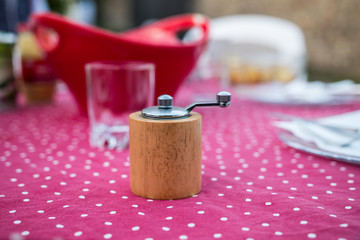 Wooden pepper mill (burr mill) close up on a table with a pink tablecloth. Very practical kitchen object. Sharp beautiful colorful image. Blurry background.