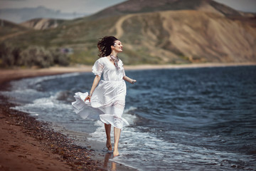 Beautiful girl, bride, in white dress, barefoot, runs on the beach, on the water and laughs. Fashion, style, wedding. Space.