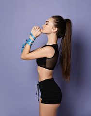Sporty girl brunette is standing in profile with her hands tied with a measure tape and fists at her chin on purple