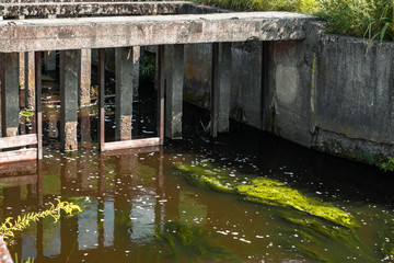 Fototapeta na wymiar A small concrete bridge across the canal with the streaming waste. Waste flow under the concrete structure of the drain manifold