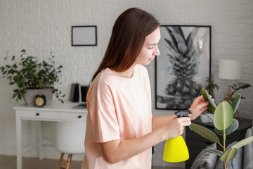 Young woman spraying water on houseplant at home
