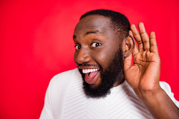 Close up photo of interested curious dark skin man hold hand near ears listen confidential promo about x-mas wonder feel impressed wear style white sweater isolated over red color background