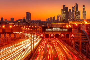 A high angle shot of an illuminated highway at sunset with the traffic light trails and a Russian...