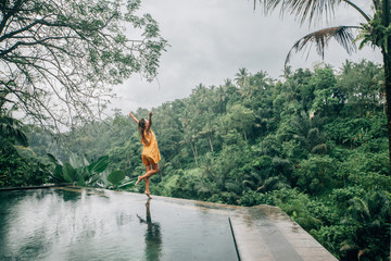 Woman enjoying tropical rain while on infinity pool on Bali