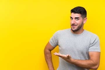 Young handsome man over isolated yellow background extending hands to the side for inviting to come