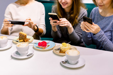 Women friends looking at cakes in cafe, making photos on the smartphones. Friends looking at photographs and laughing, cafe women, fun, enjoying