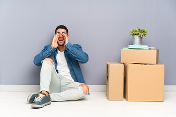 Handsome young man moving in new home among boxes shouting with mouth wide open