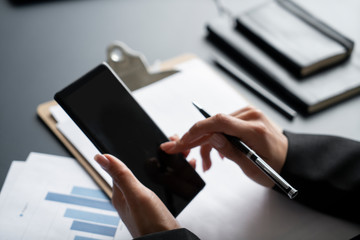 Hands of woman using smartphone at blurred office table with financial reports and graphs. Concept...