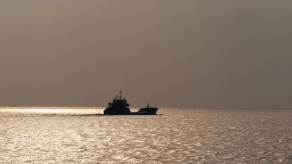Obraz premium Cargo ship sailing on ocean in the morning with sky and sea background, Silhouette ship sailing on golden shining sea.