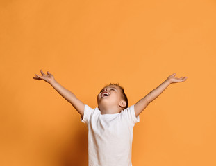 Excited kid boy in white t-shirt with his hands up wide spread is catching something. Free copy space on yellow