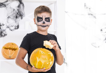 Young boy with face painted holding a pumpkin
