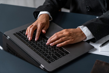 Fototapeta na wymiar Hands of African woman typing on laptop keyboard in office with blue table and documents on it. Concept of business lifestyle and education