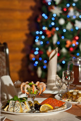 Snacks on the New Year's table, festive food, catering, reception, decor. Shrimp, fish and seafood on a festive table. Blurred Christmas tree in the background.