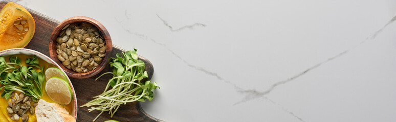 panoramic shot of autumnal mashed pumpkin soup on wooden cutting board on marble surface with copy space