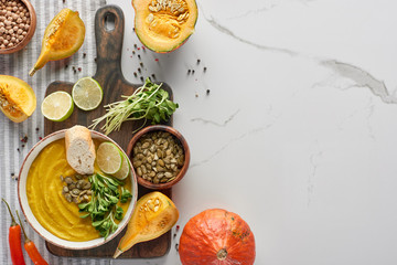 top view of seasonal mashed pumpkin soup on wooden cutting board with ingredients on marble surface
