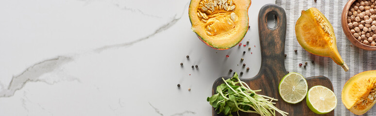top view of wooden cutting board with pumpkin, lime and sprouts on marble surface, panoramic shot