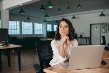 Young businesswoman thinking about work while sitting at her desk