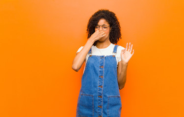 young pretty black woman feeling disgusted, holding nose to avoid smelling a foul and unpleasant...