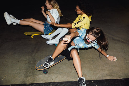 Image of amazed multinational girls riding on skateboards at night