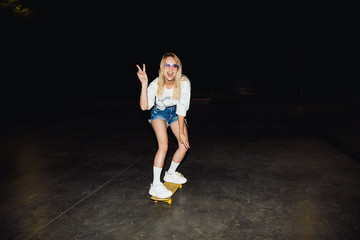 Image of blonde caucasian girl smiling and riding skateboard at night