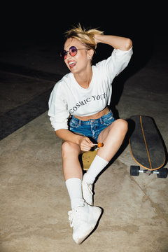 Image of blond girl eating lollipop and riding skateboard at night