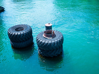 Large old black tires being used as bumpers at concrete dock, partially submerged in blue water