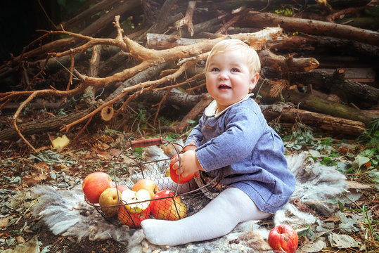 Little cute girl is sitting on the grass with a basket of apples in her hands. Plump cute baby. Autumn baby photo