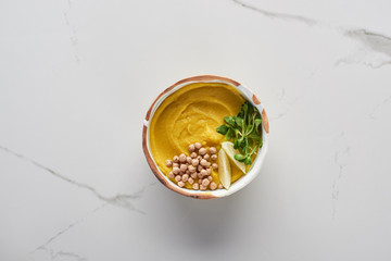 top view of autumnal mashed pumpkin soup in bowl on marble surface